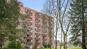 Un immeuble résidentiel à plusieurs étages, doté de balcons, d’un chemin pavé et entouré de verdure.