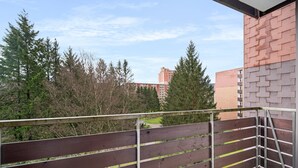Un balcon doté d’une rambarde en métal, donnant sur une zone boisée et un bâtiment en briques.