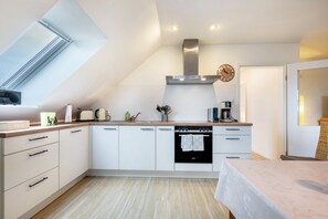 A modern kitchen with white cabinets, a built-in oven, a stainless steel range hood, and a skylight. - Apartment 'At-home-in-pellworm' with Shared Garden, Balcony and Wi-Fi (Amt Pellworm)