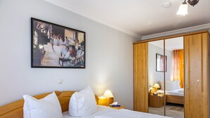 A hotel room with a bed, pillows, a nightstand, a lamp, a painting, and a wardrobe. - Apartment 'Europa' with Shared Garden, Balcony and Wi-Fi (Bad Füssing)