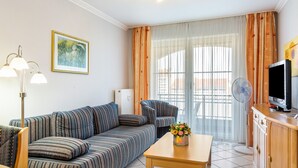 A living room with a sofa, a table with a vase of flowers, a standing fan, a television, and a radiator. - Apartment 'Europa' with Shared Garden, Balcony and Wi-Fi (Bad Füssing)