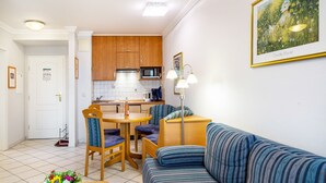 A compact living space with a kitchenette, a dining area with chairs, a sofa, and a framed picture on the wall. - Apartment 'Europa' with Shared Garden, Balcony and Wi-Fi (Bad Füssing)