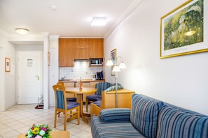 Ein gemütlicher Wohnraum mit Küchenzeile, einem Essbereich mit Stühlen, einer Couch und einem gerahmten Bild an der Wand.