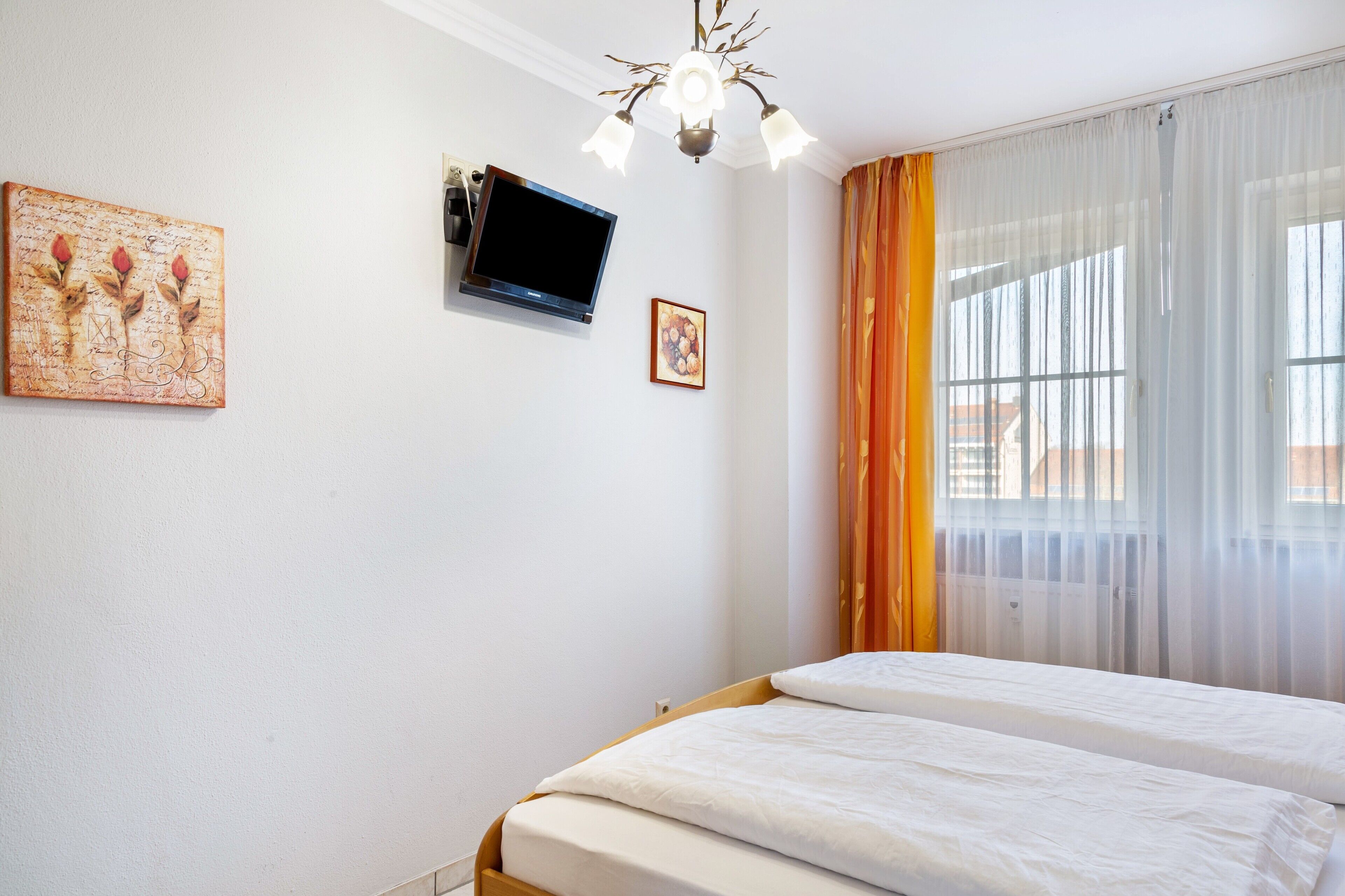 A bedroom with two beds, a television, a chandelier, and a window with curtains.