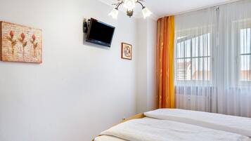 A bedroom with two beds, a television, a chandelier, and a window with curtains.