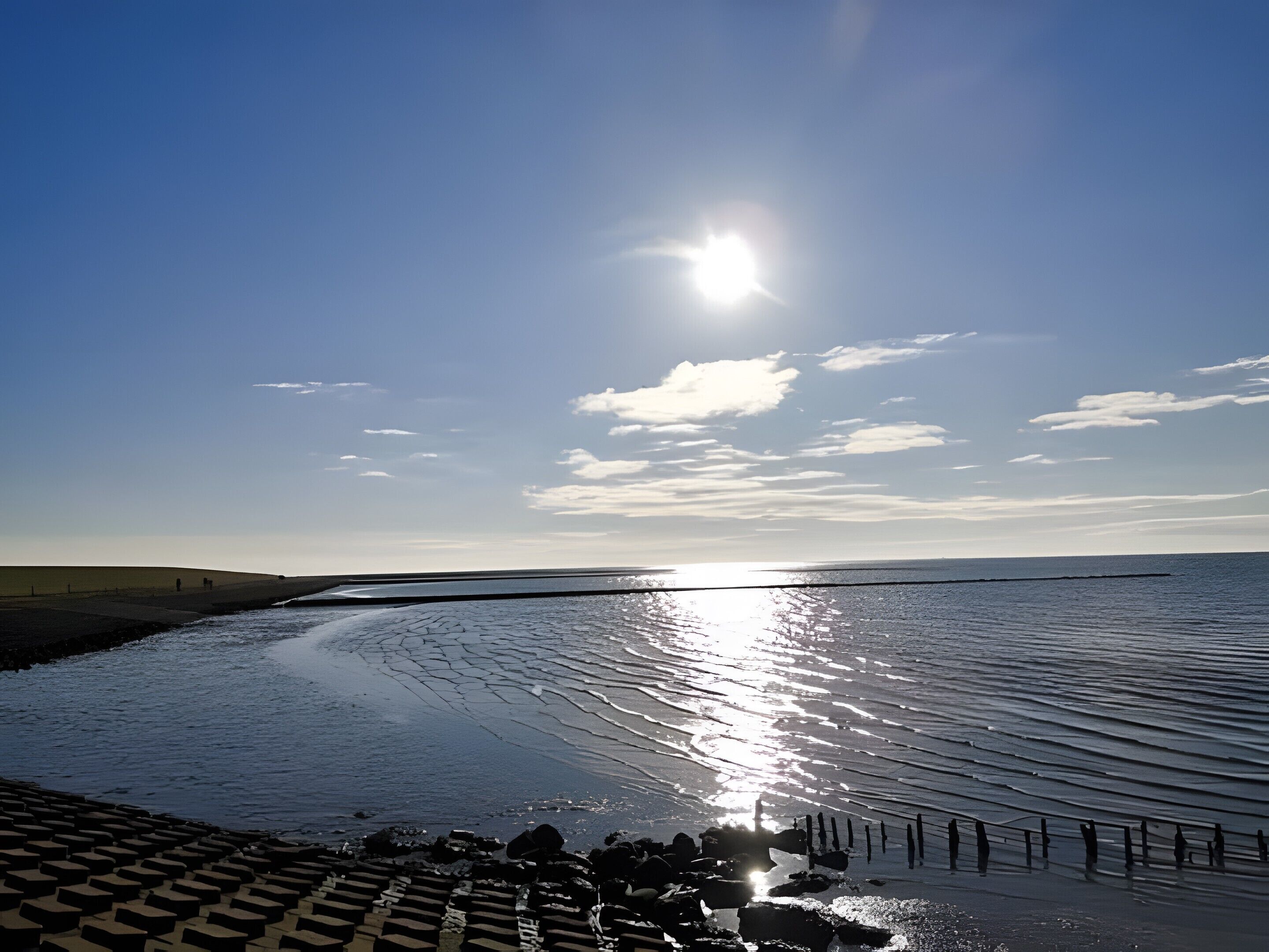 Een kustgezicht met een heldere lucht, kalme zee en een zon die in het water glinstert.