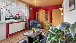 Un salon avec un radiateur, un fauteuil bleu, un meuble en bois, un canapé et une table sur laquelle se trouve un vase.