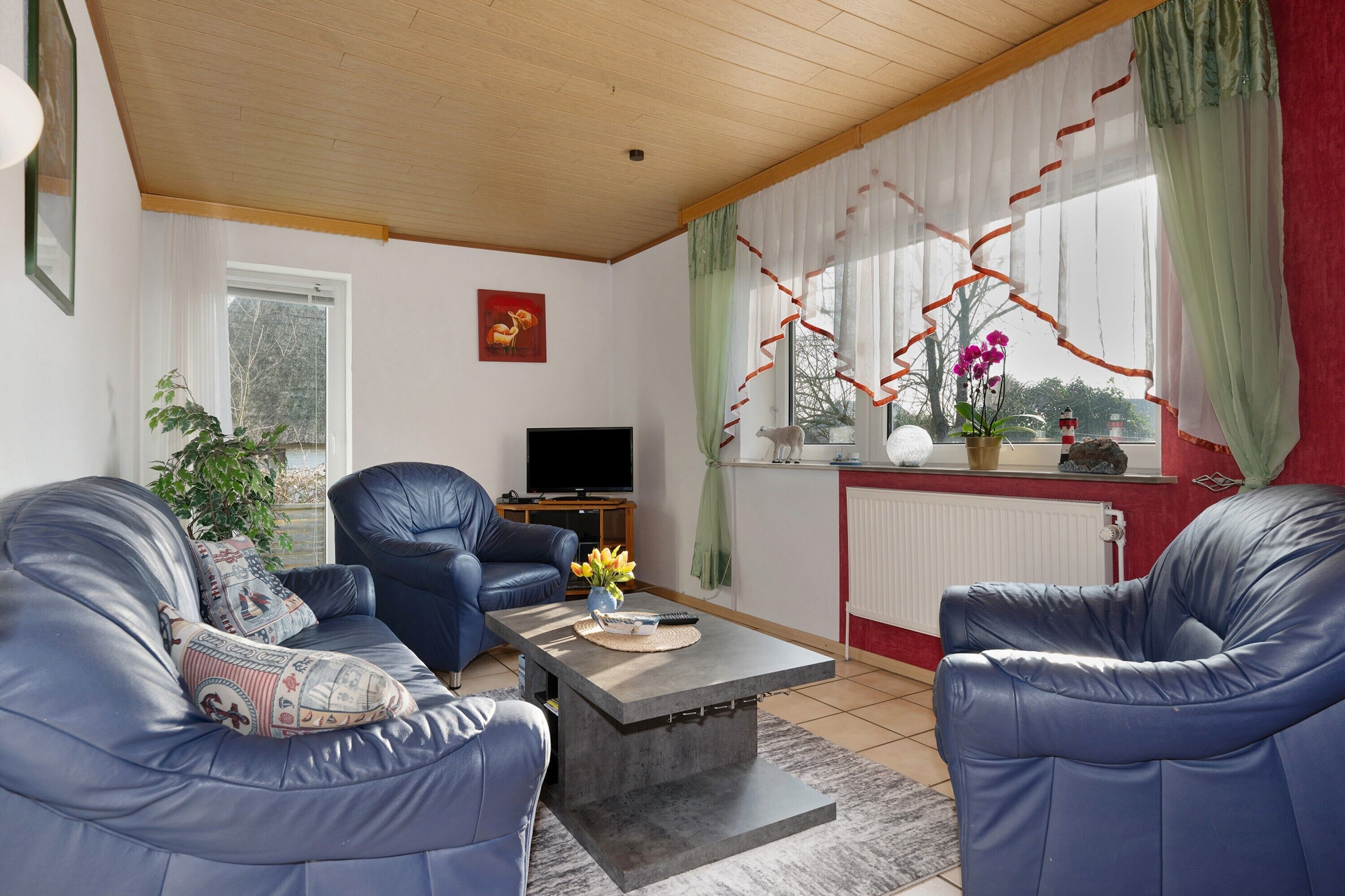 A living room with two blue leather sofas, a coffee table, a TV, and a window with curtains.