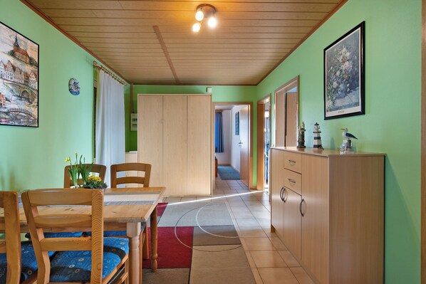 A room with a dining table, chairs, a cabinet, and a hallway leading to another room.