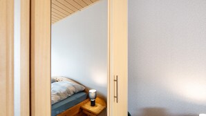 Une chambre à coucher avec un lit en bois, une table de chevet avec une lampe et une porte donnant sur une autre pièce.