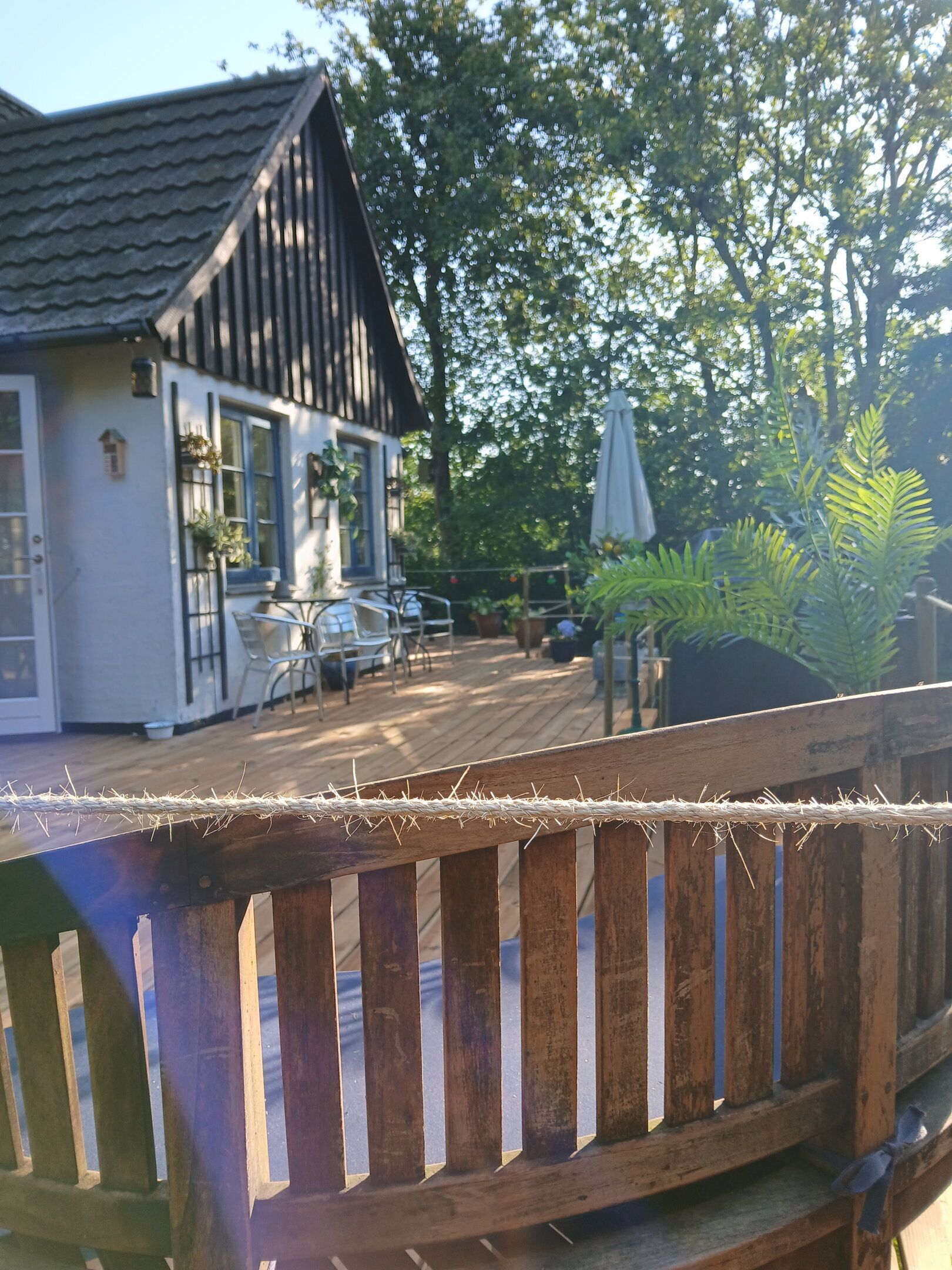 A wooden deck with a railing, a house with a tiled roof, outdoor furniture, and potted plants.