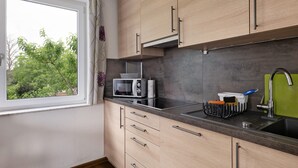 Een keuken met houten kastjes, een magnetron, een spoelbak en een raam met uitzicht op bomen.