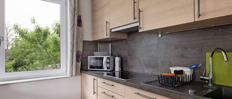 A kitchen with wooden cabinets, a microwave, a sink, and a window with a view of trees.