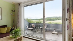 Een balkon met een tafel en stoelen, een plant en uitzicht over een groen landschap.