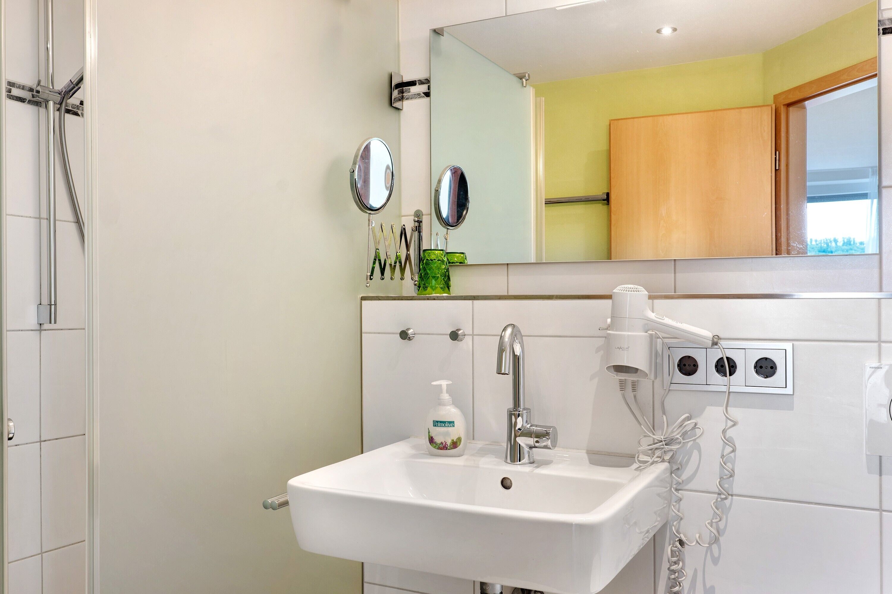 A bathroom with a white sink, a mirror, a hairdryer, and a green soap dispenser.