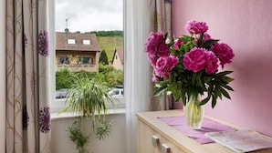 A window with curtains, a vase with flowers, and a plant on a windowsill. - Holiday Apartment 'Trollinger' with Kitchenette, Balcony, and Wi-Fi (Vaihingen an der Enz)