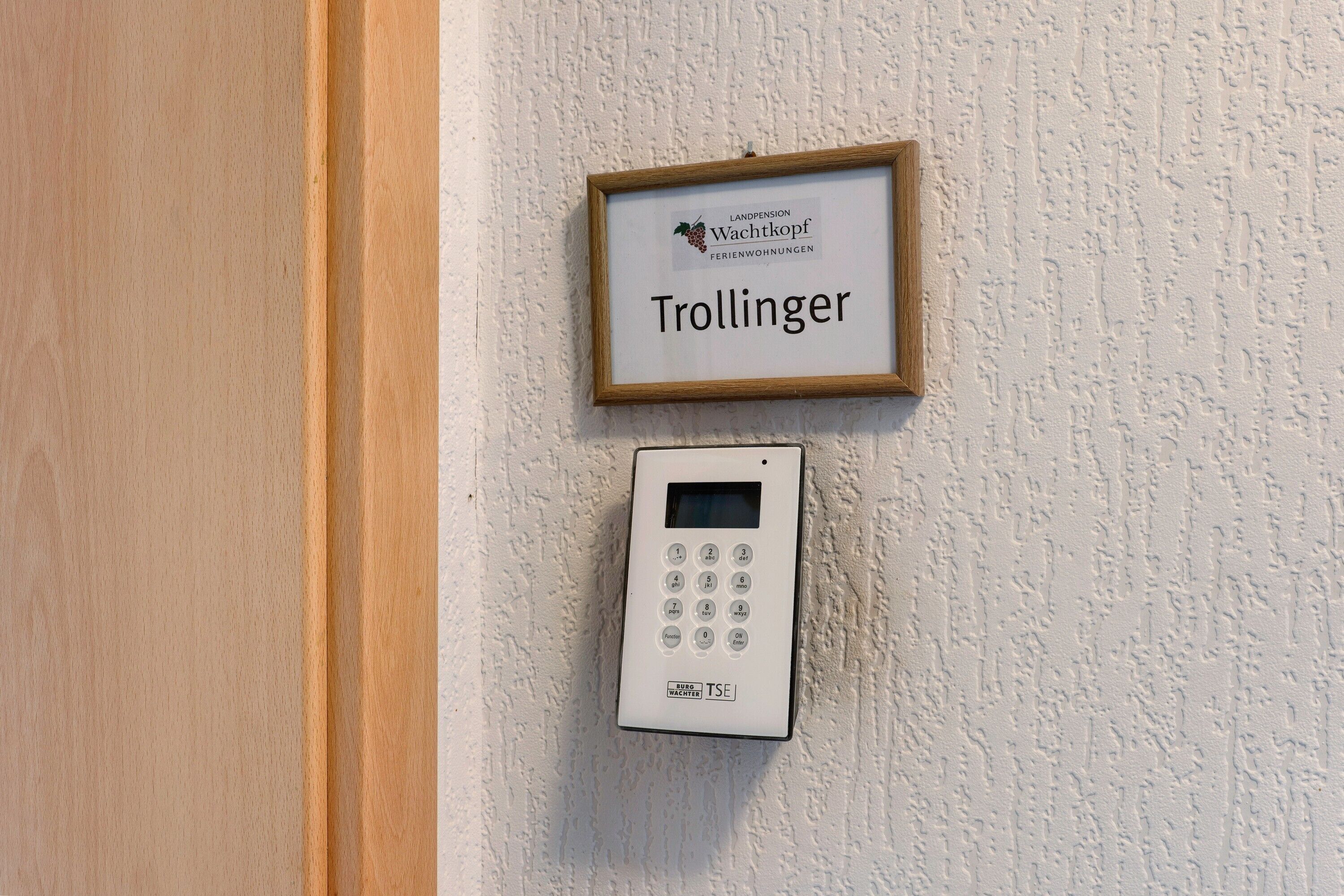 Une serrure électronique fixée au mur et une plaque décorative encadrée portant l’inscription « Trollinger » et « Landpension Wachtkopf Ferienwohnungen ».
