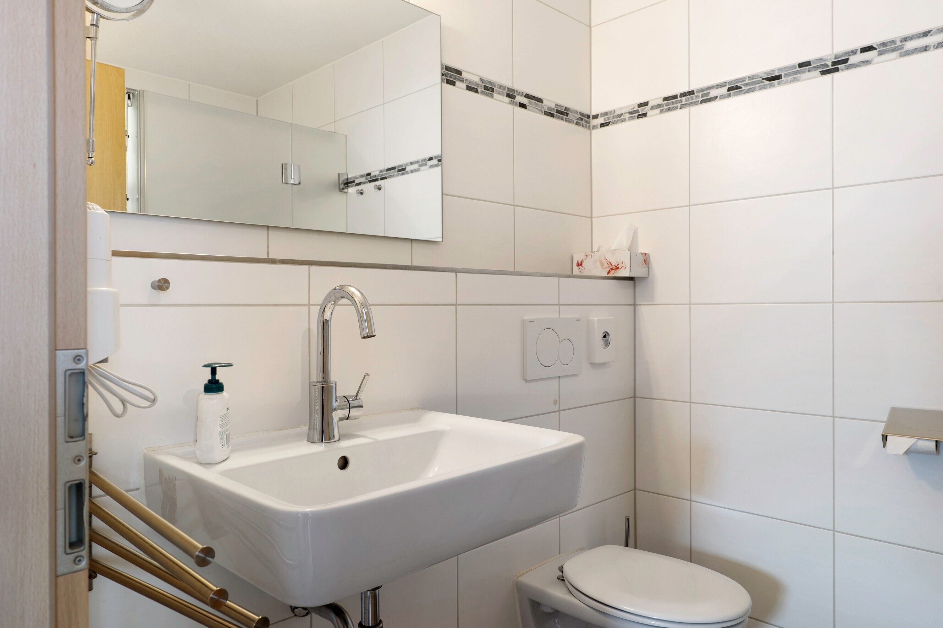 Un baño con lavamanos blanco, espejo, inodoro y zona de ducha.