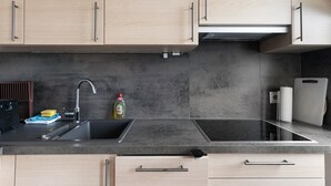 A modern kitchen with light wood cabinets, a black countertop, a stainless steel sink, and an induction cooktop. - Holiday Apartment 'Trollinger' with Kitchenette, Balcony, and Wi-Fi (Vaihingen an der Enz)