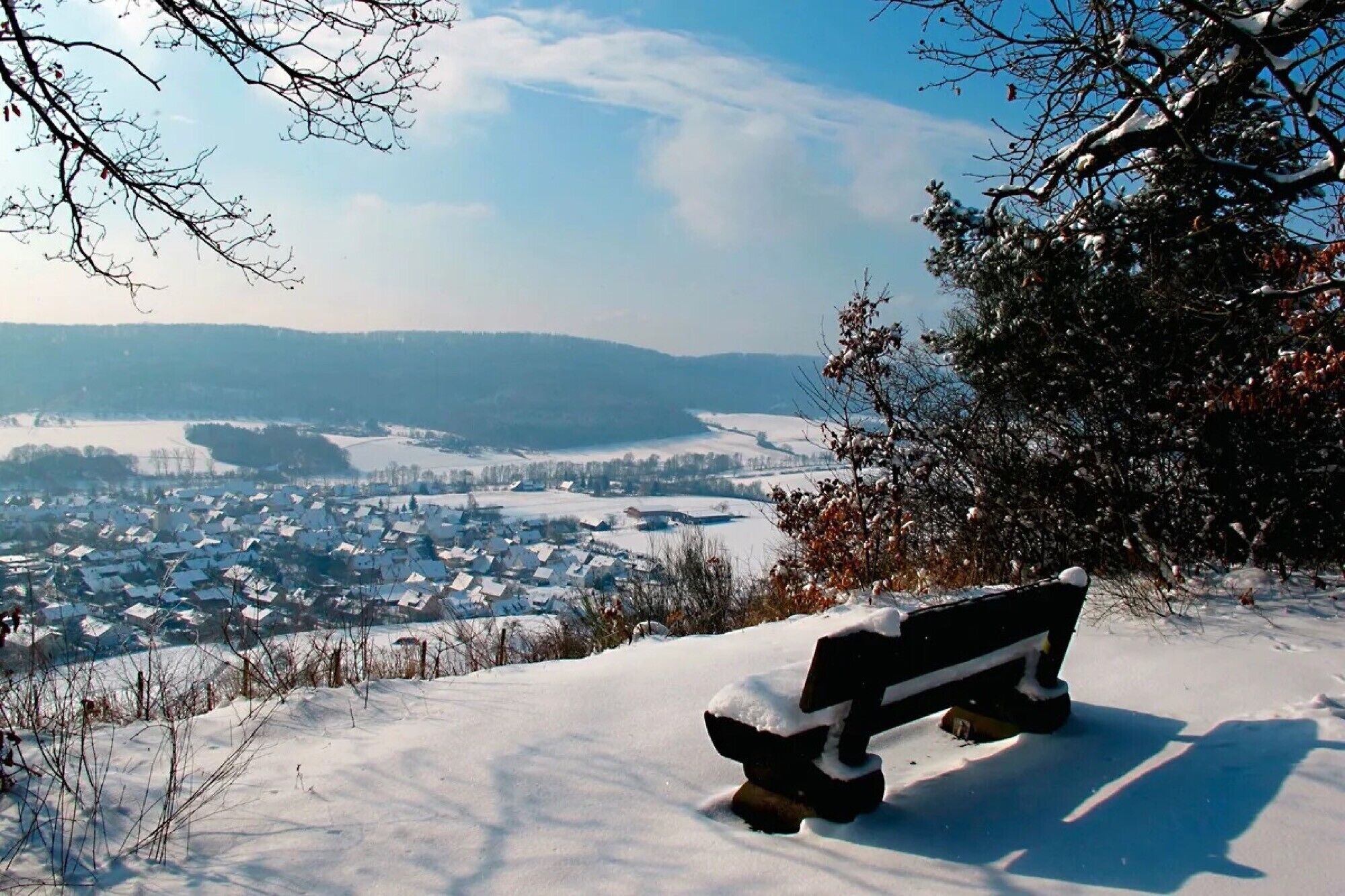 A bench on a snowy hill overlooking a town.