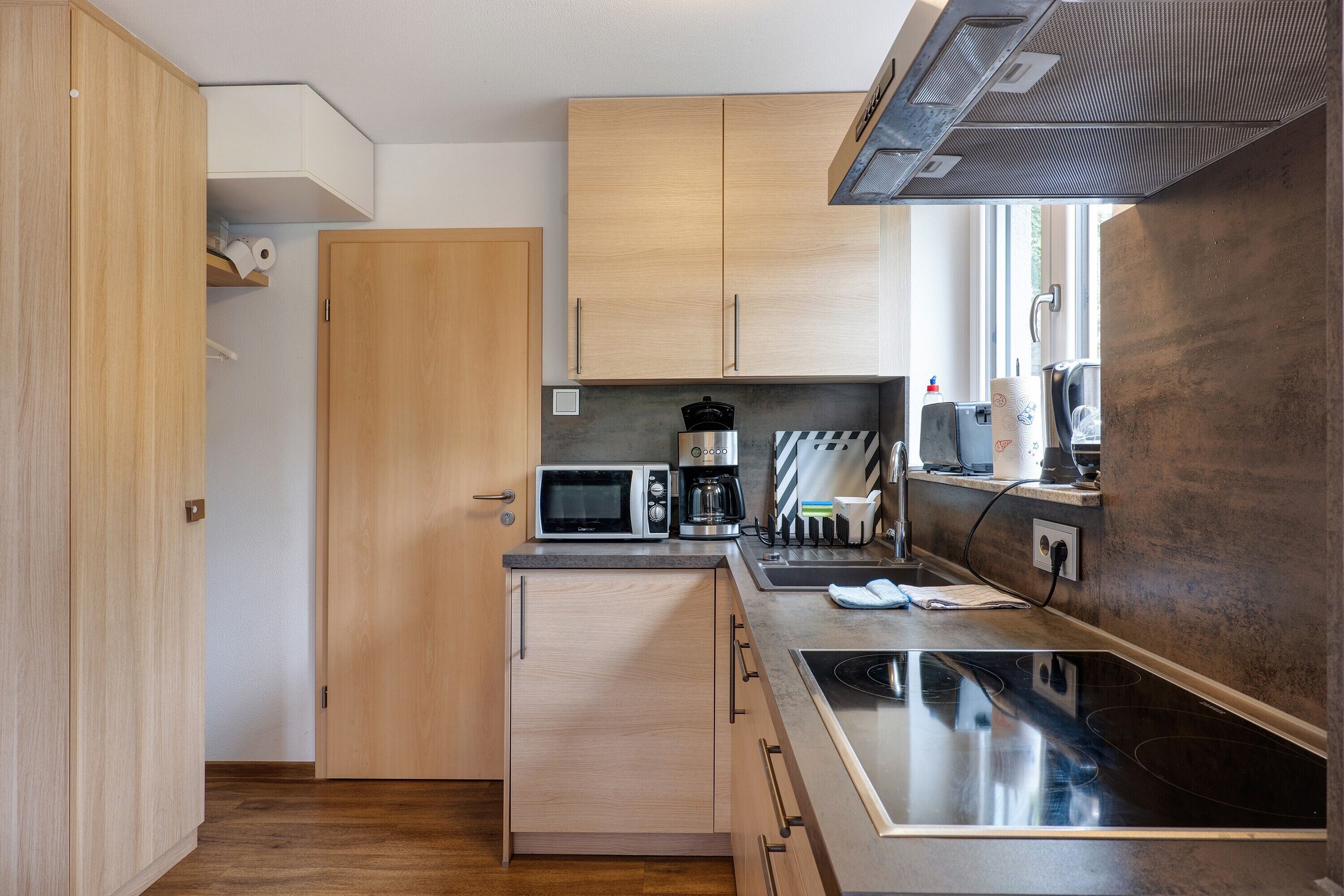 A compact kitchen with wooden cabinets, a microwave, a coffee maker, and a stove.