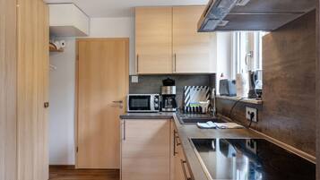 A compact kitchen with wooden cabinets, a microwave, a coffee maker, and a stove.