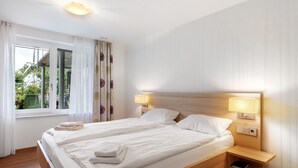 A double bed with two bedside tables, a window with curtains, and a view of greenery outside. - Apartment 'Burgunder' with Private Terrace, Kitchenette and Wi-Fi (Vaihingen an der Enz)