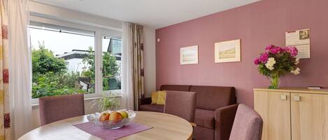 A room with a round dining table, a sofa, a cabinet, and a window with curtains.