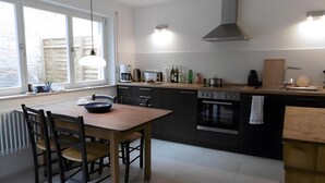 A modern kitchen with a dining table, chairs, a stove, oven, and a window with blinds. - Holiday Home 'Schlößleweg 2a' with Private Terrace, Private Garden and Wi-Fi (Bodman-Ludwigshafen)