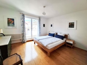 Et soveværelse med seng, skrivebord, stol, radiator og et vindue med gardiner.