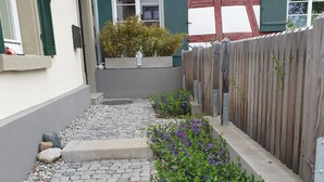 A narrow pathway leading to a house with a wooden fence, a small garden with purple flowers, and a stone-tiled area. - Holiday Home 'Schlößleweg 2a' with Private Terrace, Private Garden and Wi-Fi (Bodman-Ludwigshafen)