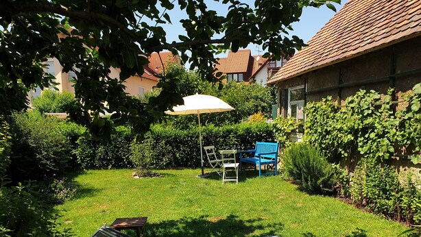 A backyard with a lawn, a striped lounge chair, a blue chair, and a table with a white umbrella. - Holiday Home 'Schlößleweg 2a' with Private Terrace, Private Garden and Wi-Fi (Bodman-Ludwigshafen)