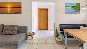 A living room with a sofa, a dining table, a wooden door, and two paintings on the walls. - Lovingly Furnished Holiday Apartment in Gaienhofen on Lake Constance (Gaienhofen)