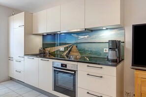 Una cocina moderna con horno empotrado, cafetera y vistas a un muelle sobre el agua.