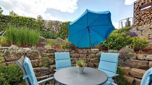 An outdoor patio with a round table, four blue chairs, a blue umbrella, and a stone wall backdrop. - Lovingly Furnished Holiday Apartment in Gaienhofen on Lake Constance (Gaienhofen)