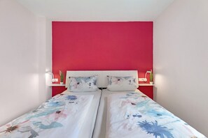 Uma cama de casal com roupa de cama florida, uma parede de destaque vermelha e mesas de cabeceira com plantas.