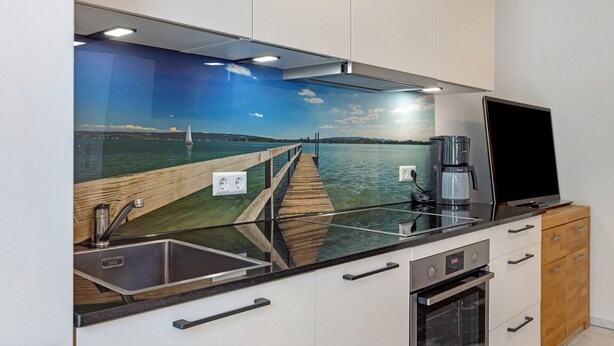 A modern kitchen with a built-in island, stainless steel appliances, and a scenic mural of a pier and water. - Lovingly Furnished Holiday Apartment in Gaienhofen on Lake Constance (Gaienhofen)