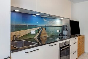 Een moderne keuken met een inbouwkookeiland, roestvrijstalen apparatuur en een sfeervol muurschildering van een pier en water.
