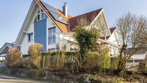 Een tweelaags huis met een schuin dak, schoorsteen en een stenen muur ervoor.