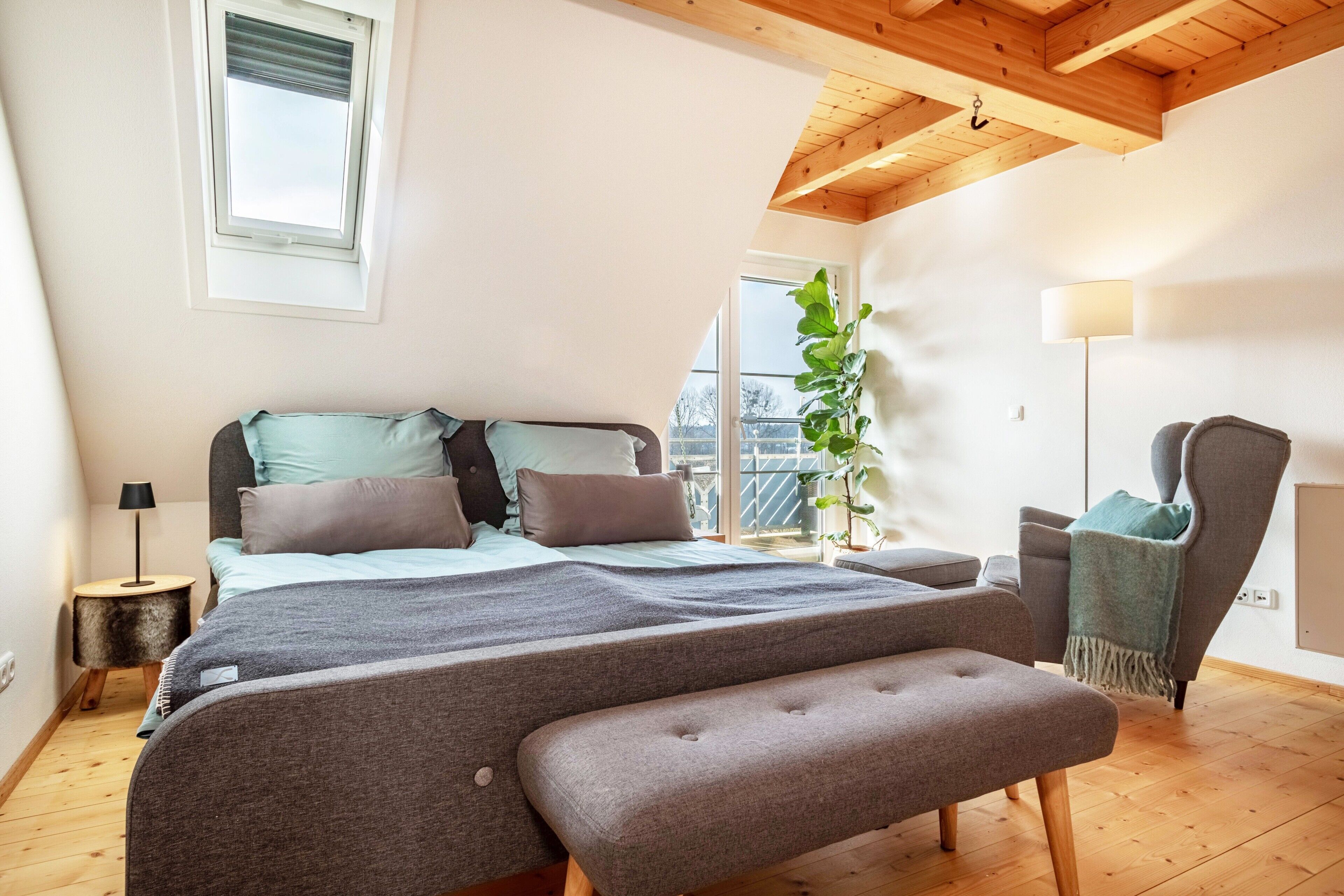 Ein Schlafzimmer mit Bett, Sitzbank, Stuhl, Lampe und Fenster.