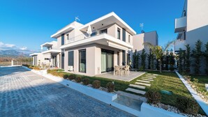 Een modern huis met twee verdiepingen, een verharde oprit, een klein terras met tuinmeubilair en een verzorgd gazon.