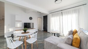 Een moderne woonkamer met een bank, een eettafel met stoelen, een televisie en een groot raam met gordijnen.
