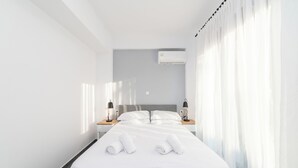Een moderne hotelkamer met een groot bed, witte lakens, twee nachtkastjes met lampen, en een raam met dunne gordijnen.