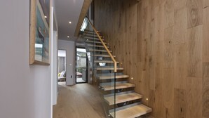 A modern staircase with glass railings and wooden steps leading to an upper floor.