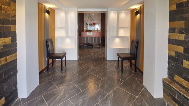 A hotel lobby with a reception desk, two chairs, and a dark tiled floor. - JKIA Boutique Inn (Syokimau)