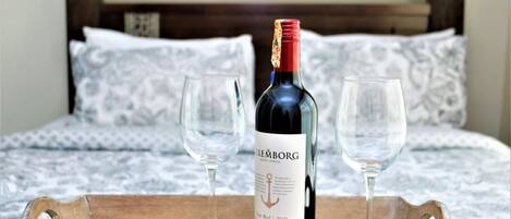 A bottle of wine on a tray with two glasses, placed on a bed with patterned bedding.