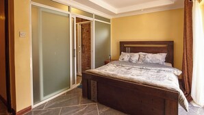 A bedroom with a wooden bed, a sliding glass door closet, and a tiled floor. - JKIA Boutique Inn (Syokimau)