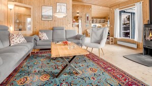 Ein gemütliches Wohnzimmer mit Holzbalkendecke, grauen Sofas, einem Couchtisch und einem gemusterten Teppich.