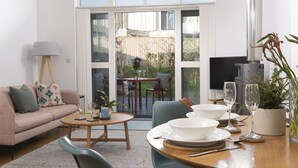 Ein modernes Wohnzimmer mit einer Couch, einem Couchtisch und einem Esstisch, der für eine Mahlzeit gedeckt ist. Im Raum befindet sich ein Fernseher und ein Kamin.