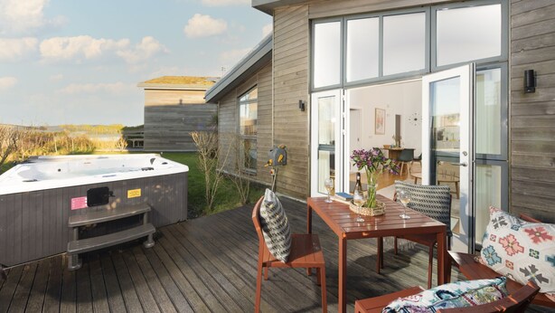 Eine Holzdiele mit Whirlpool, einem Tisch und Stühlen sowie einer Glastür, die zu einem Innenbereich führt.